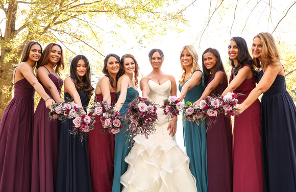 Wedding photography, the bride and bridesmaids stand together in front of yellow trees, holding out their purple bouquets. 
