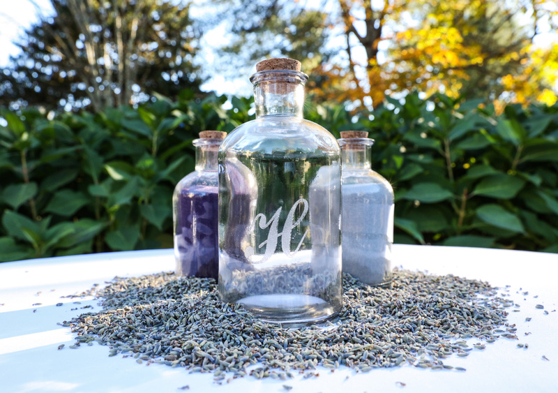 Wedding photography, three glass bottles on a table, two filled with sand, one for lavender seed.