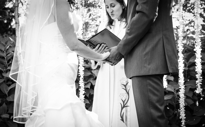 Wedding photography, a black and white close-up image of bride and groom holding hands during the ceremony. 