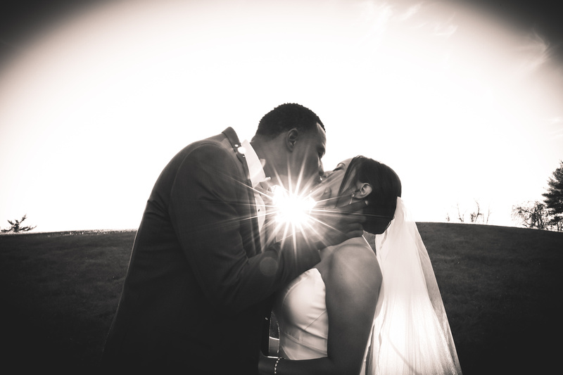 Wedding photography, a black and white image of a bride and groom kissing with a sun spot shining between their bodies. 