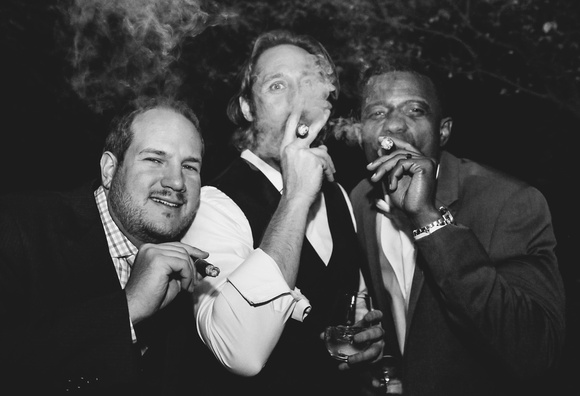 Wedding photography, a black and white image of the groom and two friends smoking cigars. 
