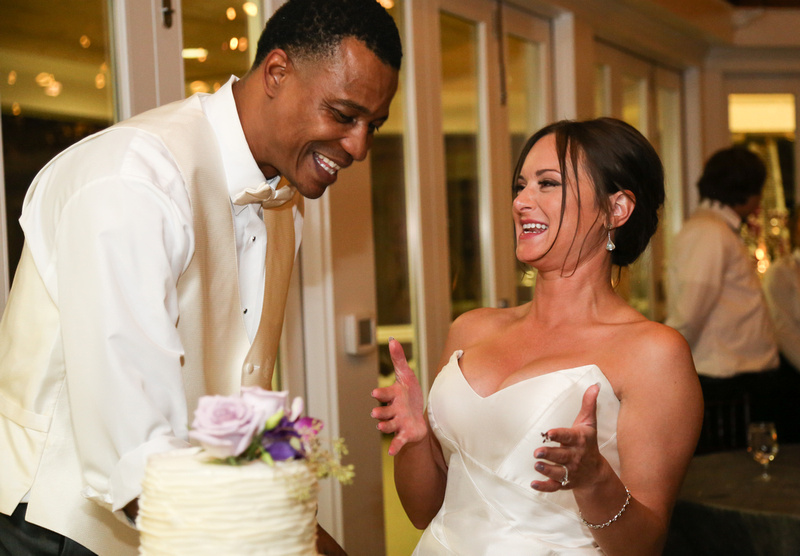 Wedding photography, the bride and groom laugh out loud while sharing their slice of cake. 
