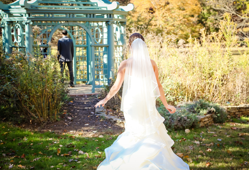 Wedding photography, a bride in a long veil and dress walks towards her groom, standing in a teal gazebo. 