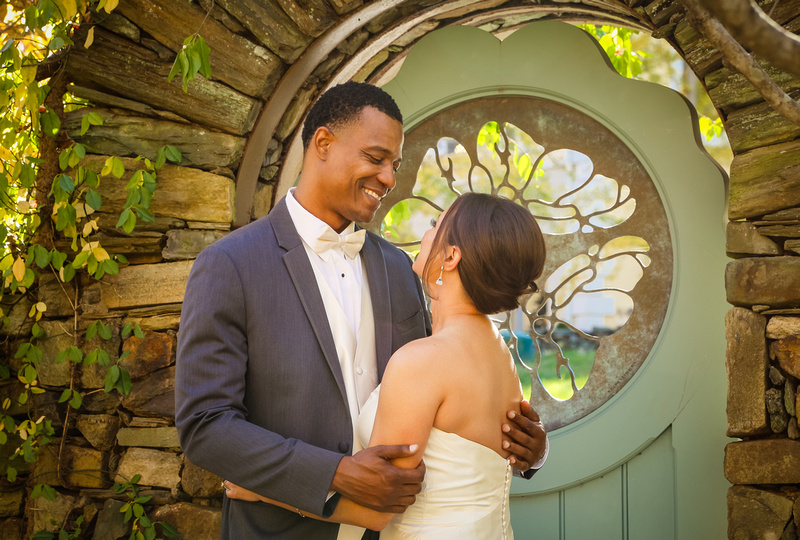 Wedding photography, a groom gazes into his bride's eyes while holding her in front of a stone wall and teal door. 