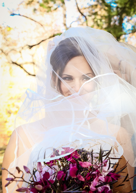 Wedding photography, the bride smiles while holding her bouquet, with her veil over her face. 