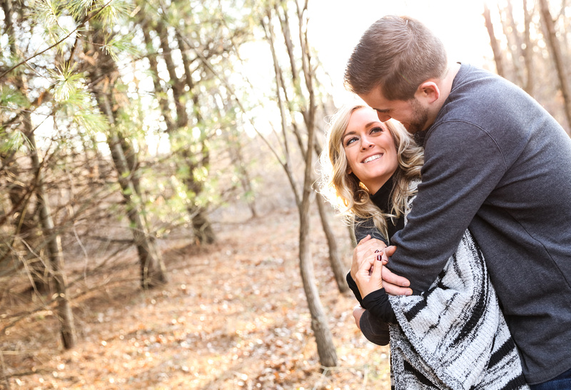 Engagement photography, a couple embraces and gaze into each other's eyes in the woods on a sunny day. 