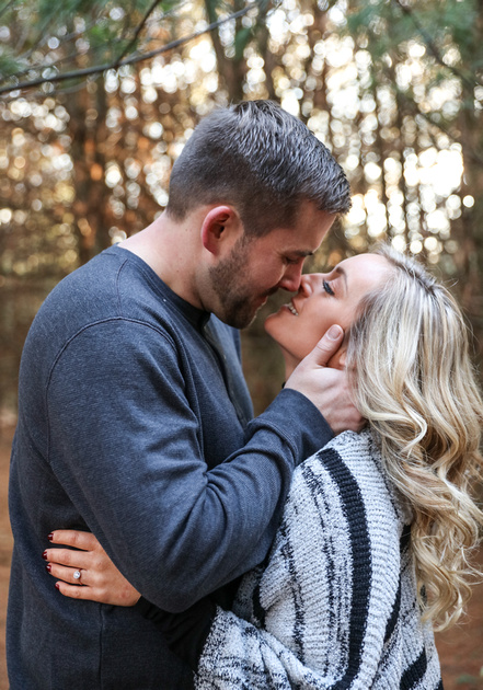 Engagement photography, a couple smiles just before they share a romantic kiss in the woods. 