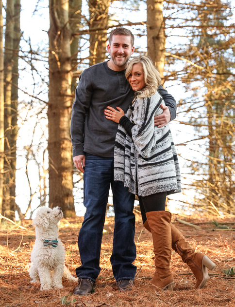 Engagement photography, a couple smiles at the camera while their small white dog looks up at them. 