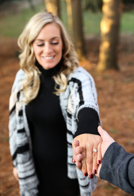 Engagement photography, a man takes his fiancé's hand, she smiles at the diamond ring on her finger. 