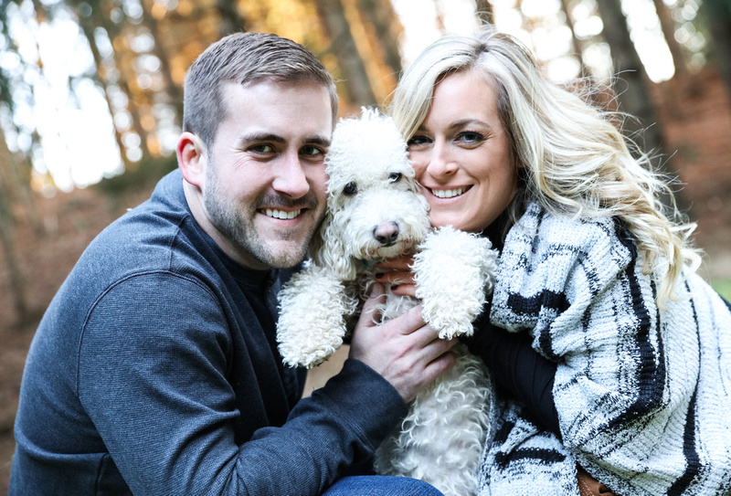 Engagement photography, a couple holds up their little white dog and smiles right next to his face. 