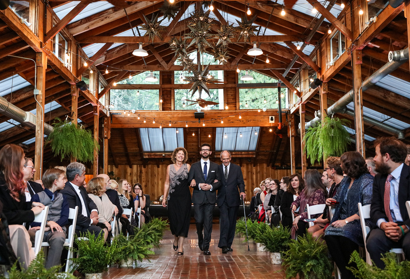 Wedding photography, a groom walks down the aisle with his parents in a elegant log cabin. 