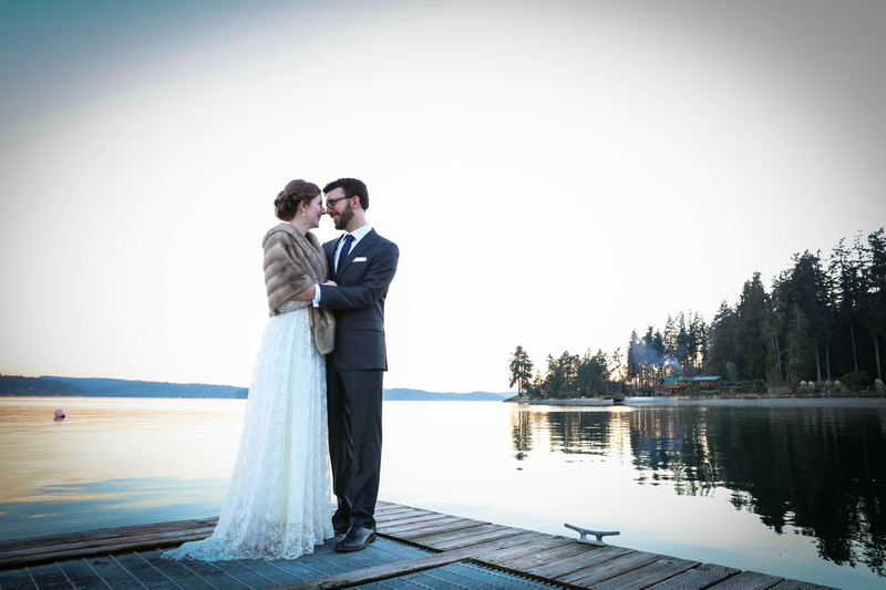 Wedding photography, a couple stands romantically on the end of a dock by the water at dusk. 