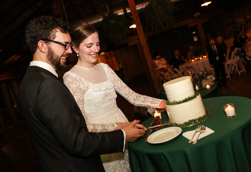 Wedding photography, a bride and groom cut their wedding cake. She wears a lace gown. 