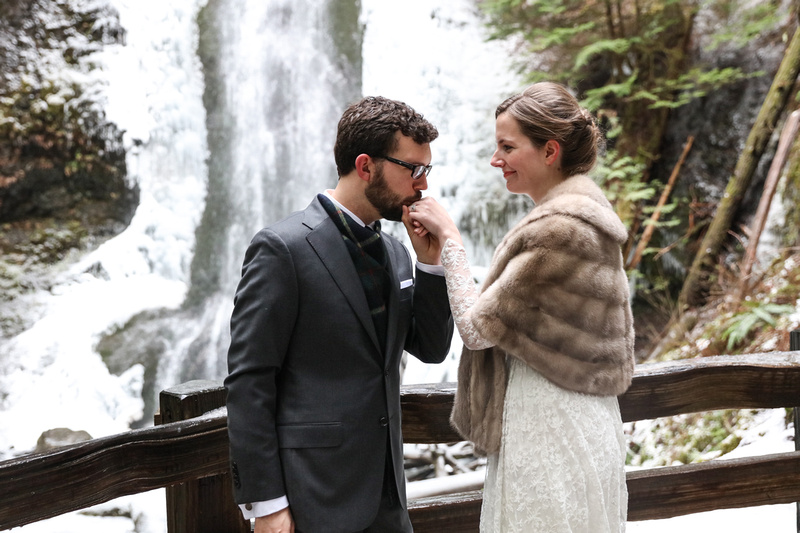 Wedding photography, a groom kisses his wife's hand in front of a winter waterfall in Washington. 