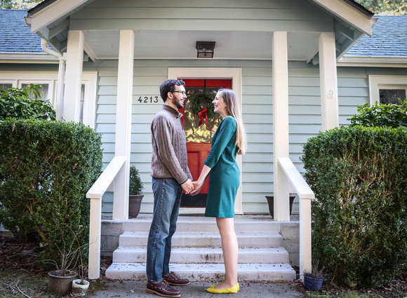 Wedding photography, a couple holds hands in front of their home. She wears a green dress. 