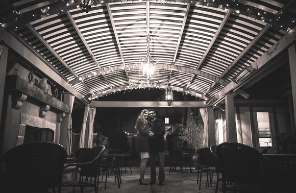 Wedding photography, a couple huddles together under a large wooden pergola. 