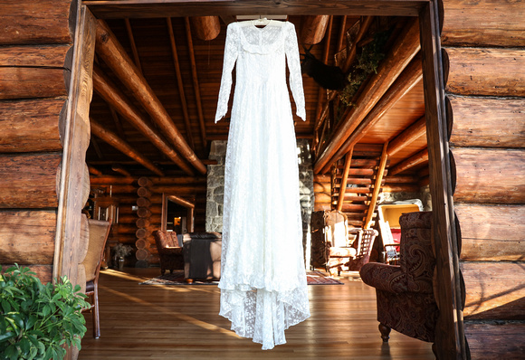 Wedding photography, a lace wedding dress hangs in the doorway of a log cabin. 