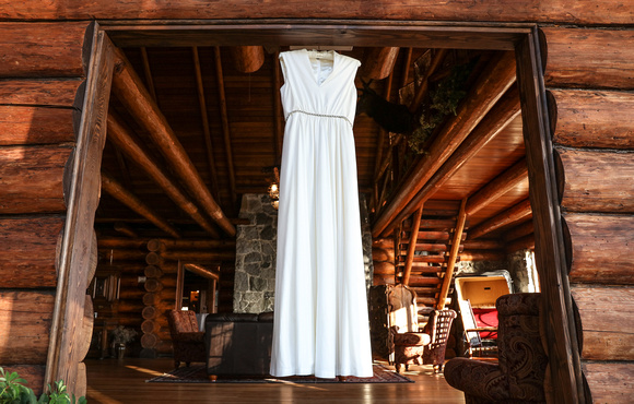 Wedding photography, a wedding dress hangs in the doorway of a log cabin. 