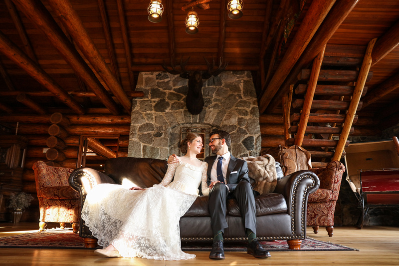 Wedding photography, a bride and groom lounge by the stone fireplace on a leather couch. 