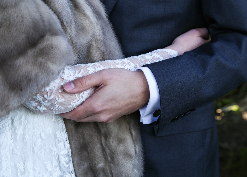 Wedding photography, a closeup of a bride and groom's arms holding each other. She wears a lace gown. 