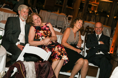Wedding photography, the parents of the bride and groom sit in chairs watching them dance. 