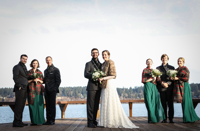 Wedding photography, a wedding party  standing on a dock by the water. They wear green and plaid. 