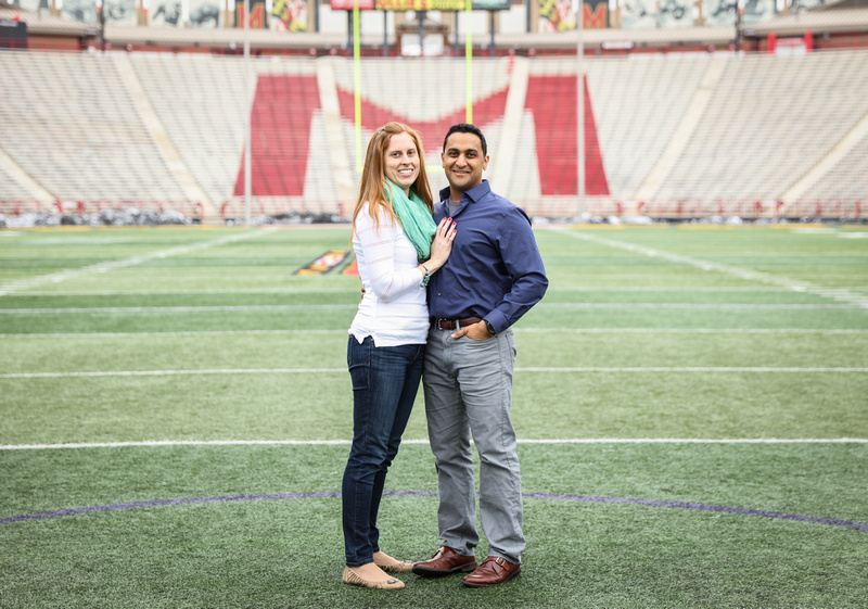 Engagement photography, a couple stands on a football field. She has red hair, he is Indian. 
