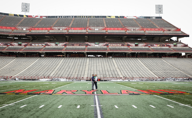Engagement photography, a couple stands together on the University of MD football field. 