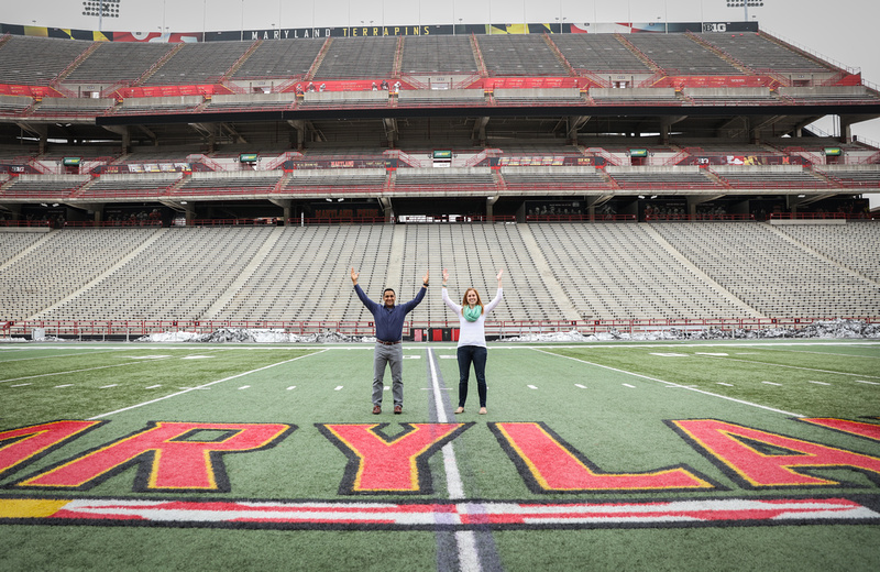Engagement photography, a couple makes the field goal symbol on the football field. 