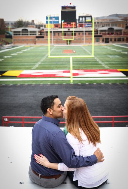 Engagement photography, a couple sits in the bleachers kissing. She has long red hair. 
