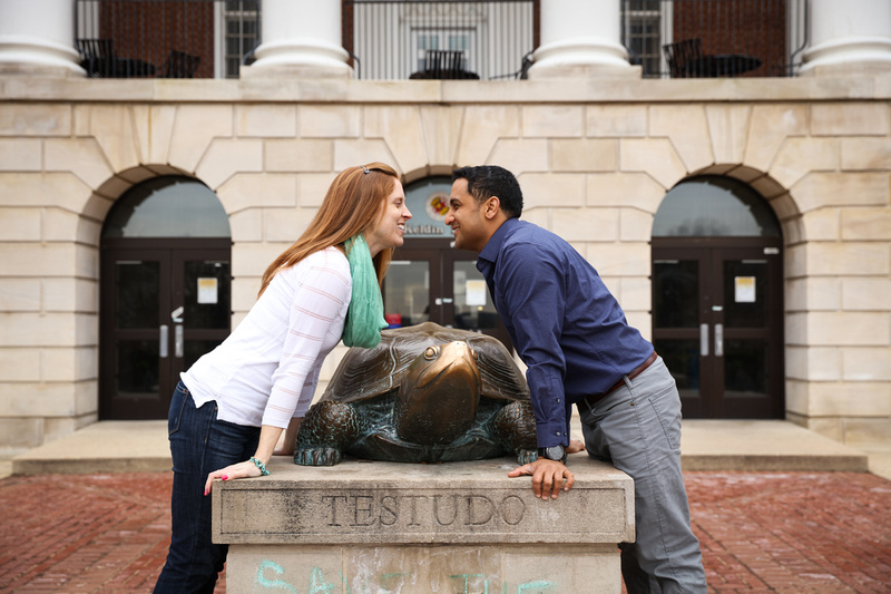 Engagement photography, a couple smiles playfully with the campus mascot statue. 
