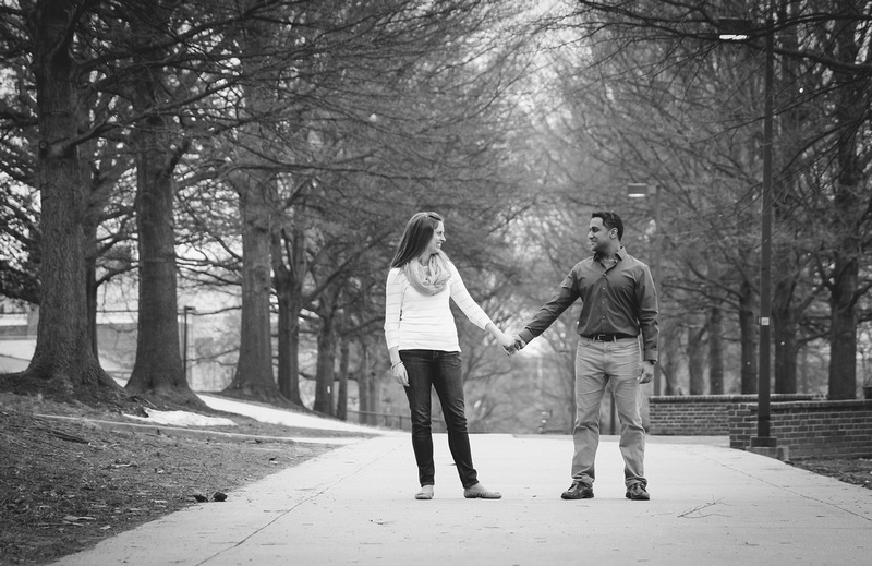 Engagement photography, a couple holds hands and looks at each other in a tree-lined pathway. 