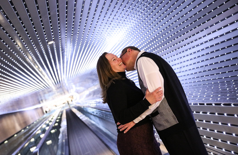 Engagement photography, a man kisses a women's neck as she laughs. They are in a light tunnel. 