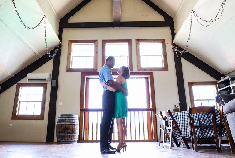 Engagement photography: a couple stands together in a barn with a big window, looking at each other lovingly. 
