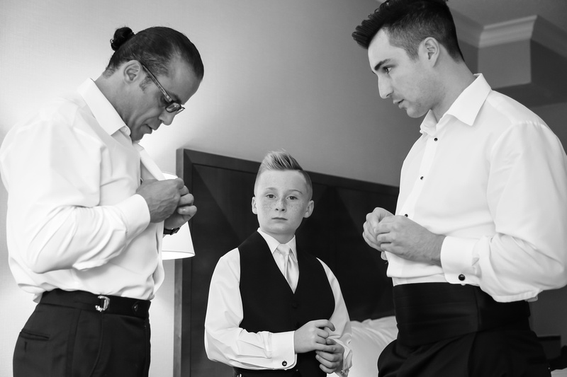 Wedding photography, a father, son, and little brother button their tuxedos on the son's wedding day. 