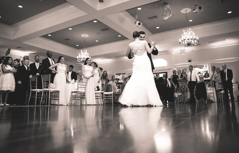 Wedding photography, a bride and groom share their first dance while guests look on lovingly. 