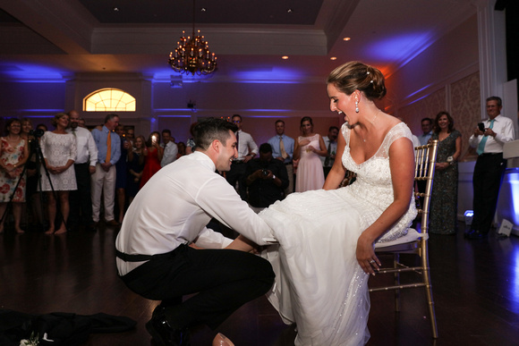 Wedding photography, the bride laughs while the groom reaches up her dress for the garter. 