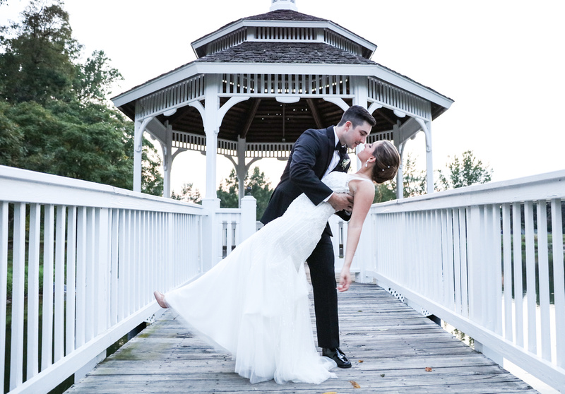 Wedding photography, a groom dips his bride while standing in front of a white gazebo. 