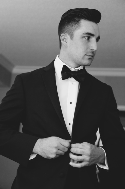 Wedding photography, a handsome dark haired groom buttons his tuxedo. 