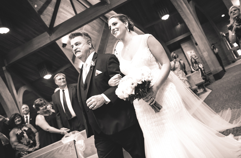 Wedding photography, a bride and her father walk down the aisle. She is smiling as she looks at her groom. 