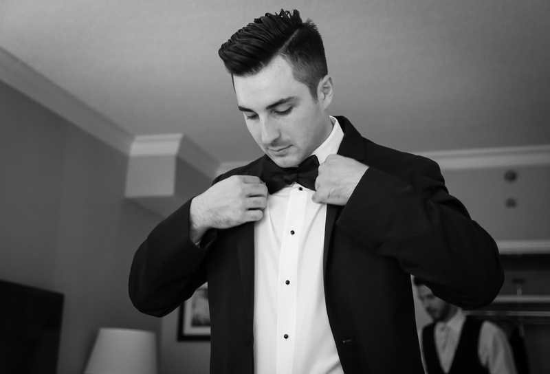 Wedding photography, a dark haired man in a tuxedo straightens his jacket. 