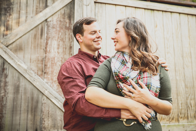 Engagement photography: a young woman in a green dress and plaid scarf smiles at her fiancé. 