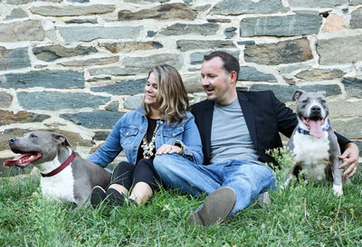 Family photography: a couple sits in front of a stone wall with their friendly pit bulls. 