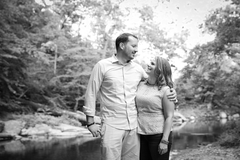 Family photography: a black and white photo of a couple embracing in front a stream in the woods. 