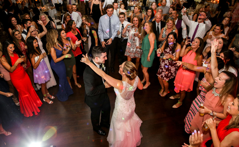 Wedding photography, a bride and groom dance while surrounded by loved ones on the dance floor. 