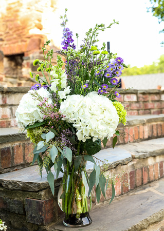 Wedding photography, a vase of white, purple, and green flowers sitting on brick stairs outside. 