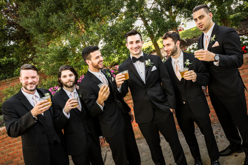 Wedding photography, a groom and his groomsmen wearing black tuxedos toast their cocktails. 