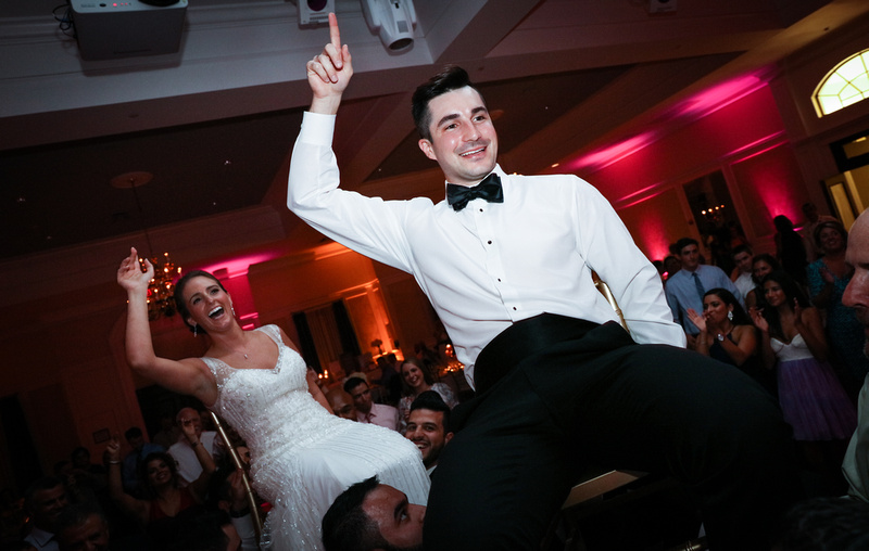 Wedding photography, a bride and groom celebrate while being lifted up on chairs. 