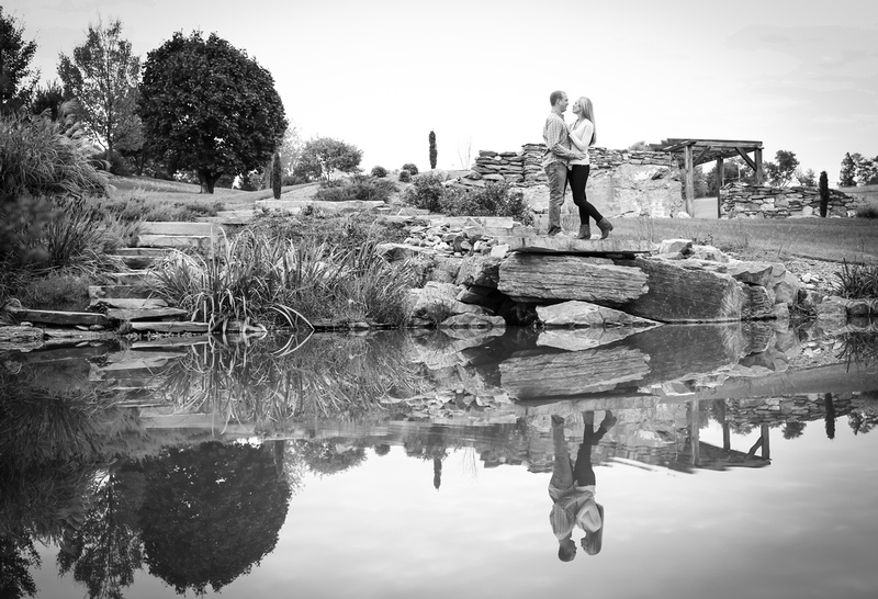 Engagement photography, a couple embraces romantically in front of a still pond. 