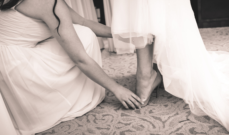 Wedding photography, a bridesmaid helps slip on the shoe of a bride. 